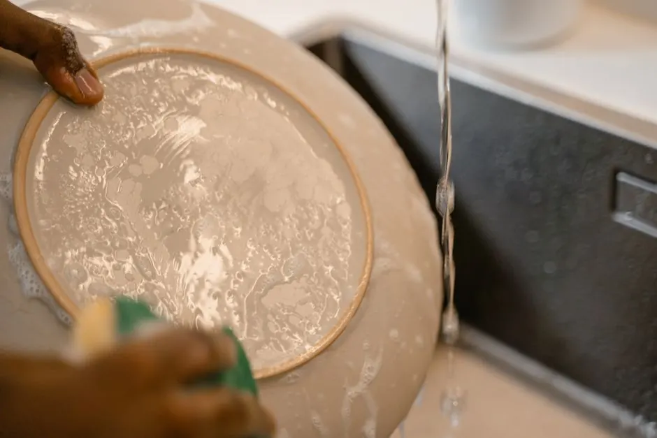 A person handwashing a ceramic plate under flowing water in a kitchen sink. Household cleaning concept.