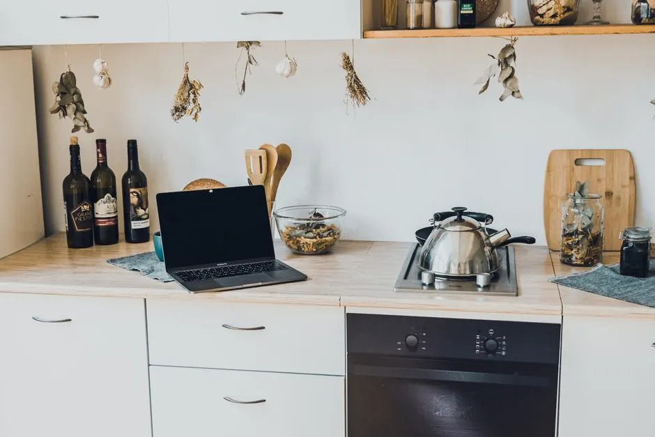 A stylish kitchen interior featuring a laptop, cookware, and decorative elements like hanging herbs.